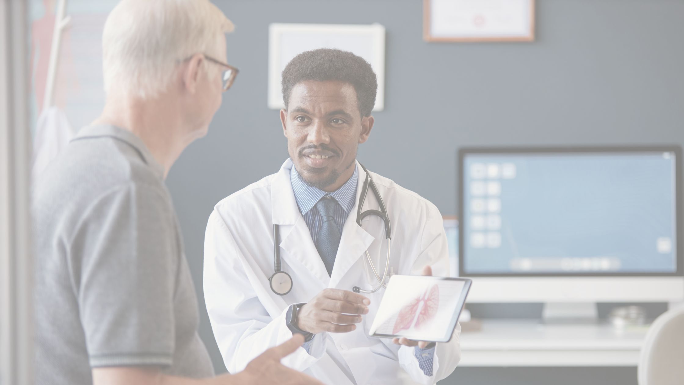 A doctor holds a tablet with a picture of lungs and speaks with a patient in an exam room
